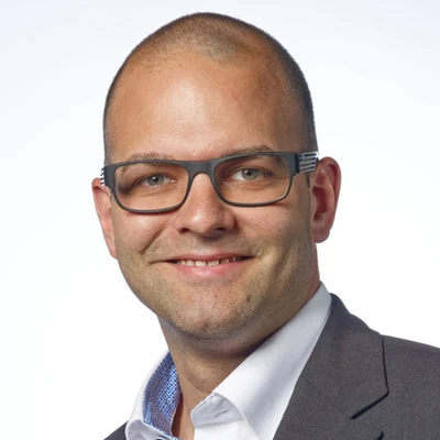 Markus Scheffknecht mit Brille und Anzug, lächelnd vor einem hellen Hintergrund.