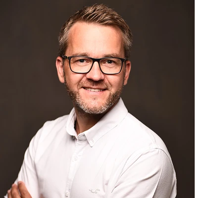 Markus Müller, ein Mann mit Brille und Bart, trägt ein weißes Hemd und lächelt freundlich in die Kamera.