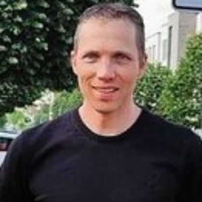 Simon Stippich steht im Freien mit einem schwarzen T-Shirt und lächelt in die Kamera.